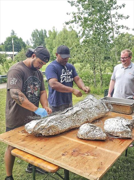 Timothy Nanai and Sika Ulutoa, YWAM Tribal Waves, left and center, unwrap a pig that was roasted the night before the celebration as Life for the Nations pastor Chad Hoffman looks on. 