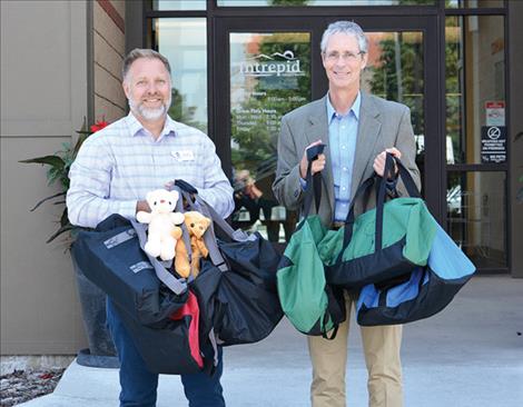 Rob Lawler, of the DPHHS Office of Faith and Community Based Services, and Intrepid CEO Greg Strizich with some of the donated duffel bags. 